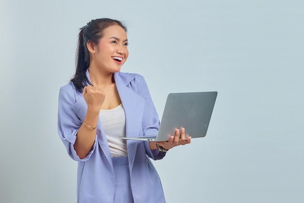 Retrato de una joven asiática sonriente sosteniendo un portátil y celebrando el éxito aislado de fondo blanco