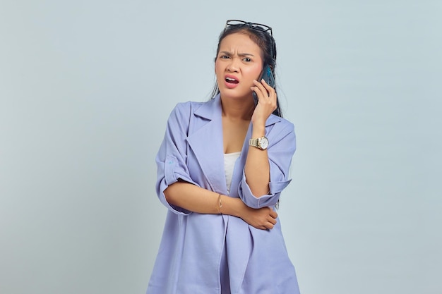 Retrato de una joven asiática sorprendida hablando por teléfono móvil y mirando hacia adelante aislada de fondo blanco