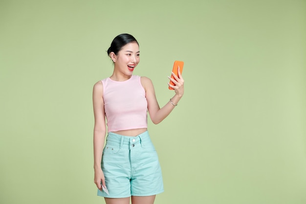 Retrato de una joven asiática sorprendida usando un teléfono móvil con fondo verde