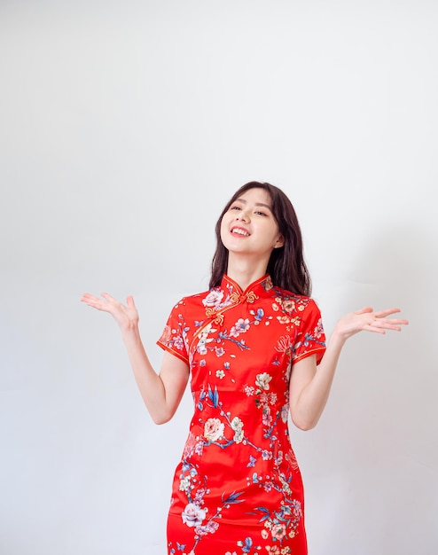 Retrato de una joven asiática con un vestido tradicional cheongsam qipao sobre un fondo blanco aislado sosteniendo un espacio de copia con dos manos