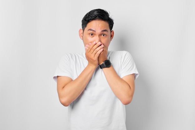 Retrato de un joven asiático asustado que cubre la boca con dos manos aislado de fondo blanco