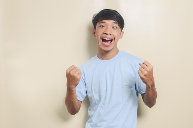 Retrato de un joven asiático con camiseta azul con expresión emocionada sobre un fondo aislado