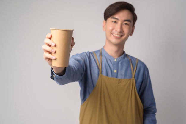 Retrato de un joven asiático con delantal sosteniendo un vaso de papel sobre blanco