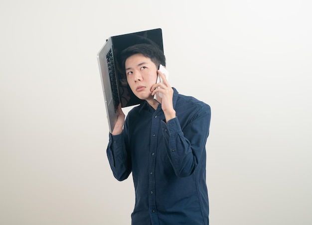 Retrato joven asiático hablando de teléfono inteligente o teléfono móvil y mano sujetando el portátil sobre fondo blanco.