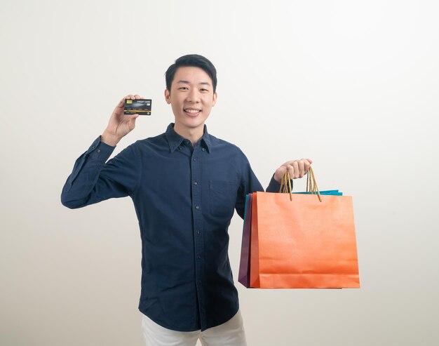 retrato, joven, asiático, hombre, tenencia, tarjeta de crédito, y, bolsa de compras, blanco, plano de fondo