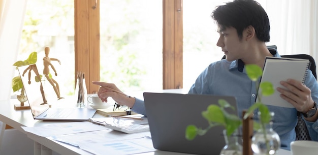 Retrato de un joven asiático independiente está trabajando en su trabajo en una tableta de computadora en una oficina moderna. Haciendo un informe de análisis contable. Datos de inversión inmobiliaria. Concepto de sistemas financieros y fiscales.