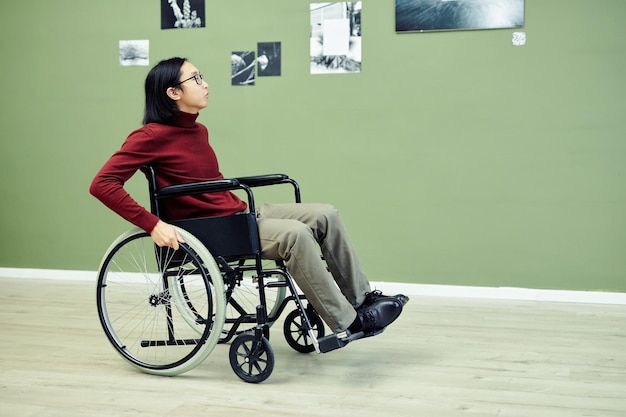 Retrato de un joven asiático moderno con discapacidad en silla de ruedas visitando una exposición de fotografía abstracta en una galería de arte