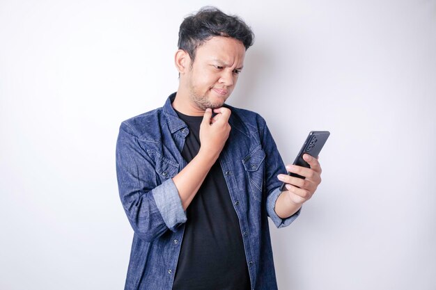 Retrato de un joven asiático pensativo con camisa azul marino mirando a un lado mientras sostenía un teléfono inteligente