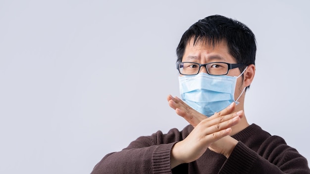 Retrato de un joven asiático que dice no a la infección por coronavirus con una mascarilla facial azul quirúrgica médica aislada en un fondo blanco de cerca
