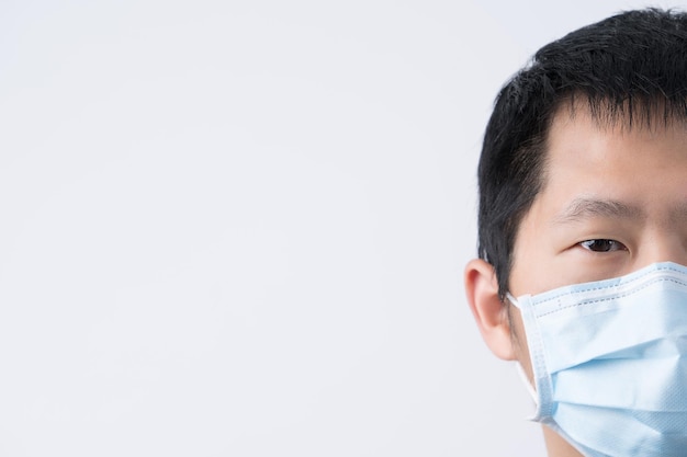 Retrato de un joven asiático que se siente enfermo usando una máscara facial azul quirúrgica para prevenir la contaminación del aire por infección aislada en el fondo blanco cortado