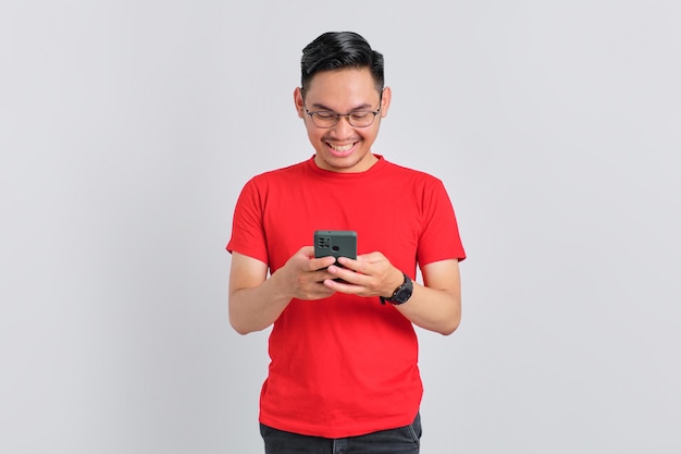 Retrato de un joven asiático sonriente usando un teléfono móvil para escribir mensajes SMS aislados sobre fondo blanco