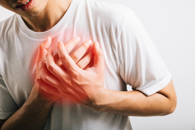 Retrato de un joven asiático sosteniendo sus brazos alrededor de su pecho sufriendo debido a un ataque al corazón estudio aislado fondo blanco estilo de vida feliz hombres dolor en el pecho salud incomodidad corazón