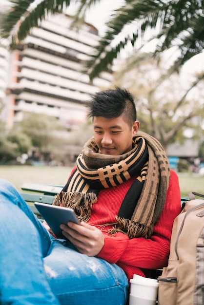 Retrato de joven asiático con su tableta digital mientras está sentado en un banco al aire libre. Concepto de tecnología.