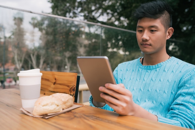 Retrato de joven asiático con su tableta digital mientras está sentado en una cafetería. Concepto de tecnología.