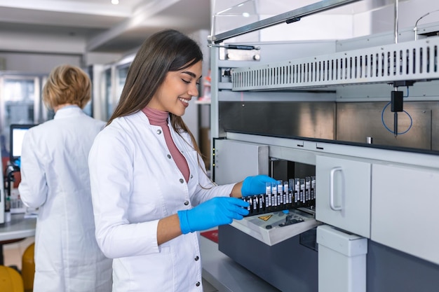 Retrato de una joven asistente de laboratorio haciendo análisis con tubos de ensayo y máquinas analizadoras sentadas en el laboratorio moderno