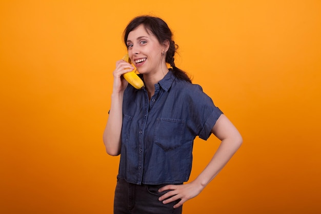 Retrato de una joven asombrada sosteniendo fruta de plátano fresca en un estudio sobre un fondo amarillo. Hermosa mujer joven con sabroso plátano.