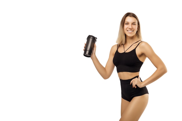 Retrato de una joven atleta hermosa mujer con un cuerpo en forma perfecta sostiene un agitador con agua o un batido de proteínas y bebe de él aislado en un fondo blanco Foto con lugar para texto