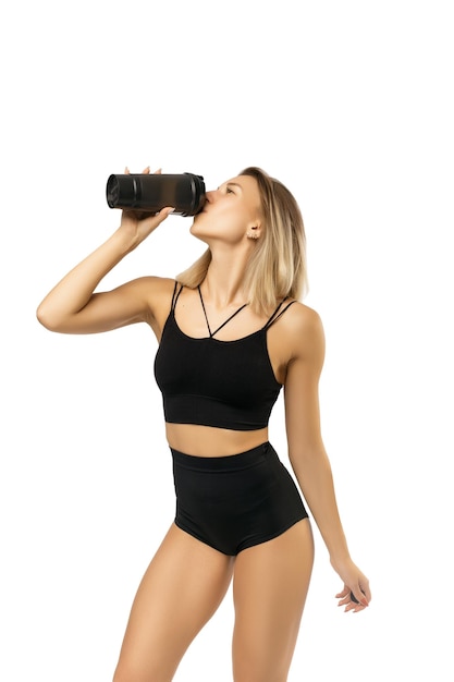 Retrato de una joven atleta hermosa mujer con un cuerpo en forma perfecta sostiene una coctelera con agua o un batido de proteínas aislado en una foto de fondo blanco con lugar para el texto