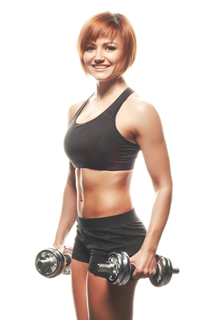 Retrato de joven atleta pelirroja mirando y sonriendo a la cámara mientras sostiene pesas.Fondo blanco, aislado, Foto de estudio