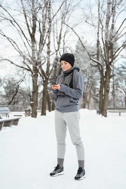 Retrato de una joven atleta que usa un teléfono inteligente durante su entrenamiento de invierno en el parque nevado de la ciudad