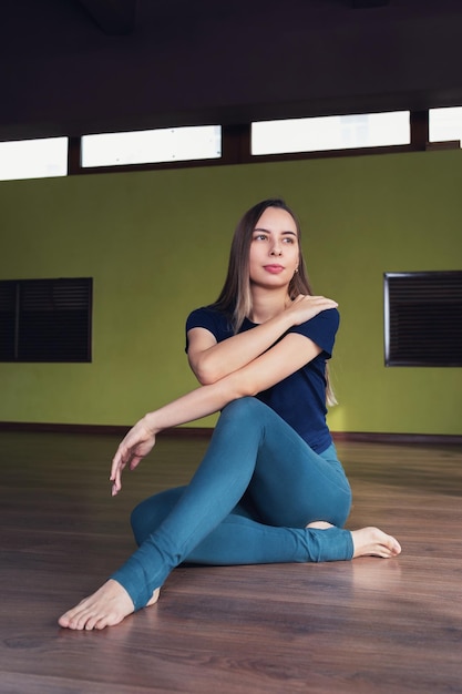 Retrato de una joven atlética sentada en el suelo con leggings y una camiseta en el gimnasio