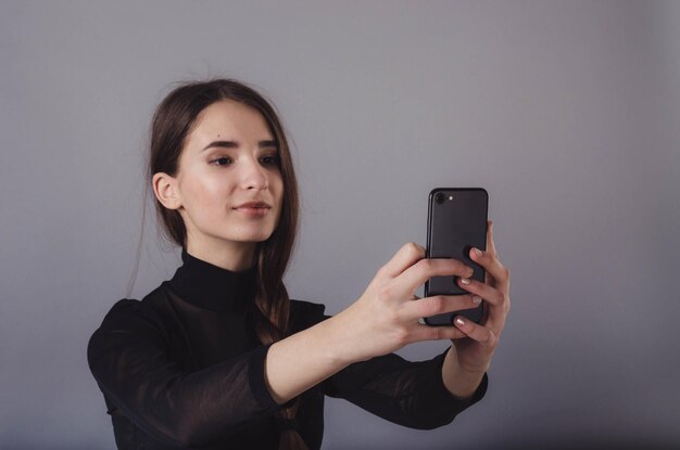 Retrato de una joven atractiva haciendo una foto selfie con un smartphone aislado en un fondo gris neutro