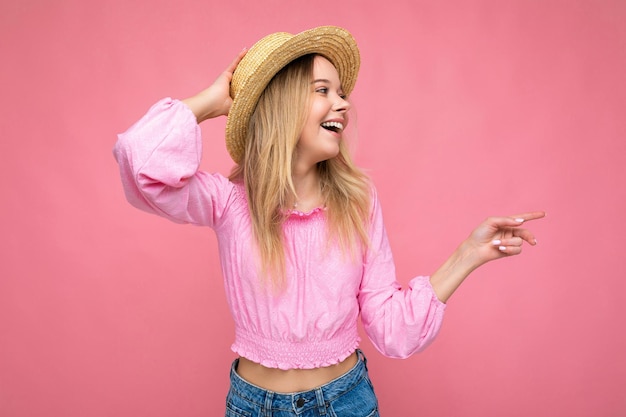 Retrato de joven atractiva mujer rubia hipster sonriente en elegante top rosa y sombrero de paja