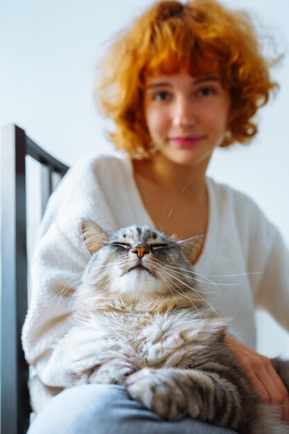 Retrato de una joven atractiva de pelo rojo con un gato doméstico esponjoso