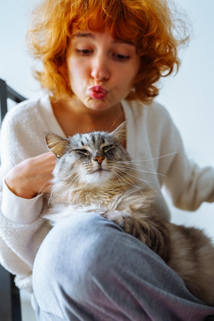 Retrato de una joven atractiva de pelo rojo con un gato doméstico esponjoso