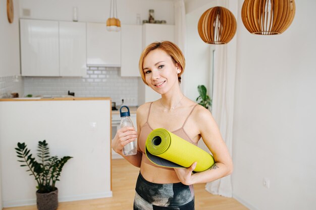 Retrato de una joven atractiva posando con estera de yoga y un vaso de agua