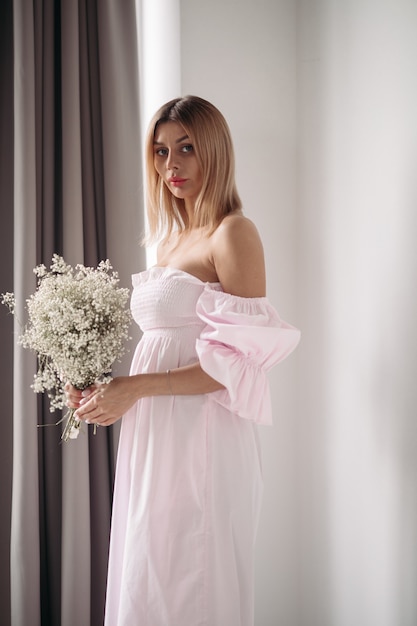 Retrato de joven atractiva en vestido blanco sosteniendo un boquet de flores blancas