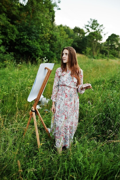 Retrato de una joven atractiva con un vestido largo pintando con acuarela en la naturaleza