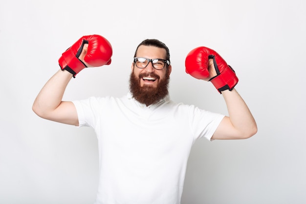Retrato de joven barbudo con camiseta blanca celebrando la victoria y con guantes de boxeo rojos