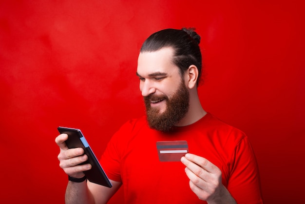 Retrato de joven barbudo con tableta y pago en línea con tarjeta de crédito