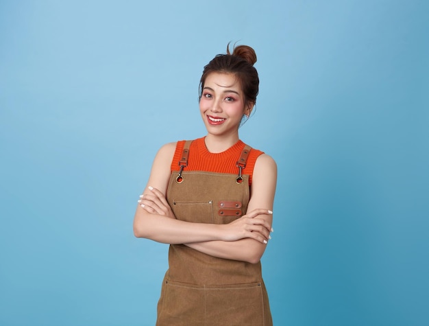 Foto retrato de una joven barista asiática con un delantal de pie y una sonrisa con los brazos cruzados