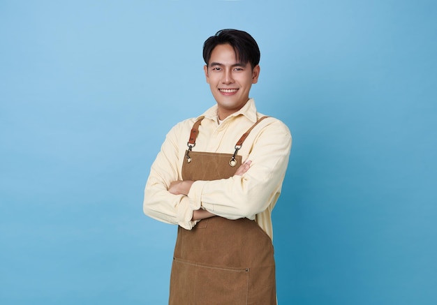 Foto retrato de un joven barista asiático que lleva un delantal de pie y sonríe con los brazos cruzados