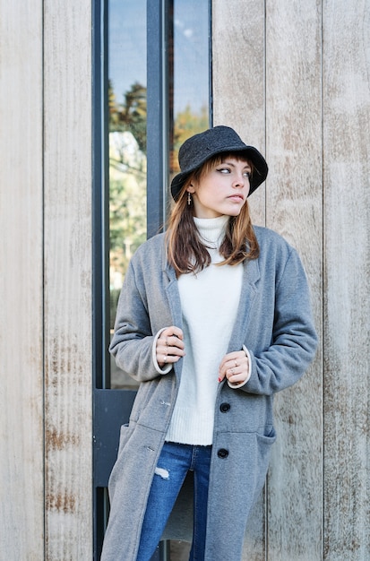 Un retrato joven bastante caucásica, vestida con una chaqueta gris, un suéter blanco y un sombrero.