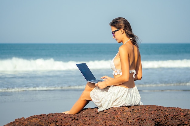 Retrato de una joven y bella chica independiente corriendo en la playa con una computadora portátil. mujer de negocios de vacaciones. concepto de autónomo y trabajo.