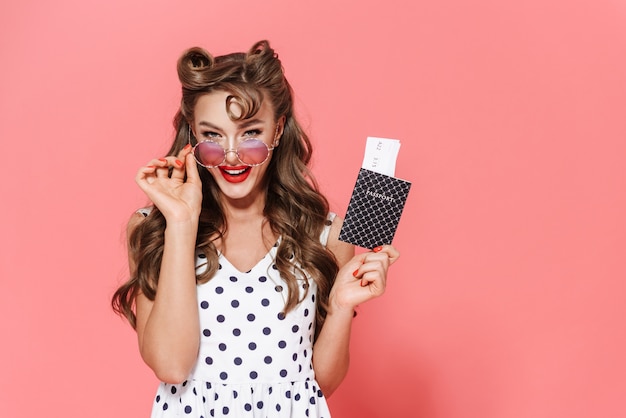 Retrato de una joven y bella chica pin-up con un vestido que se encuentran aisladas, mostrando el pasaporte con el billete de avión