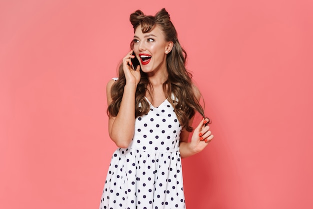 Retrato de una joven y bella chica pin-up con un vestido que se encuentran aisladas, mediante teléfono móvil