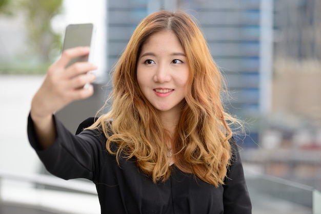 Retrato de joven bella empresaria asiática contra la vista de la ciudad al aire libre