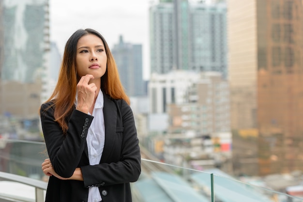 Retrato de joven bella empresaria asiática contra la vista de la ciudad