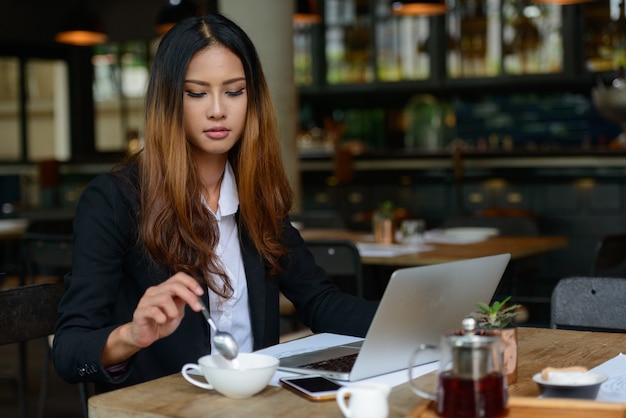 Retrato de joven bella empresaria asiática trabajando en la cafetería.