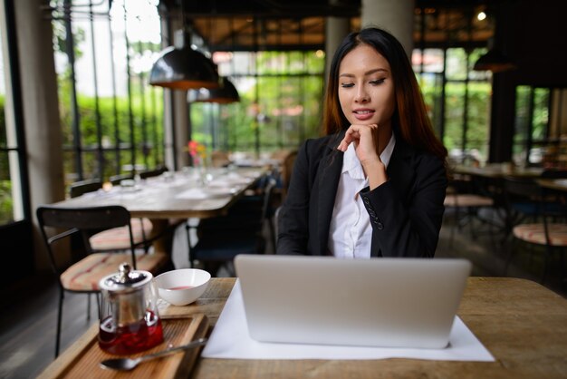 Retrato de joven bella empresaria asiática trabajando en la cafetería.