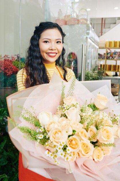 Retrato de joven y bella floristería vietnamita de pie con un gran ramo de rosas blancas