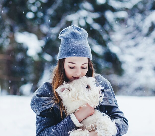 Retrato de joven bella mujer abrazando a perro terrier blanco en Winter Park