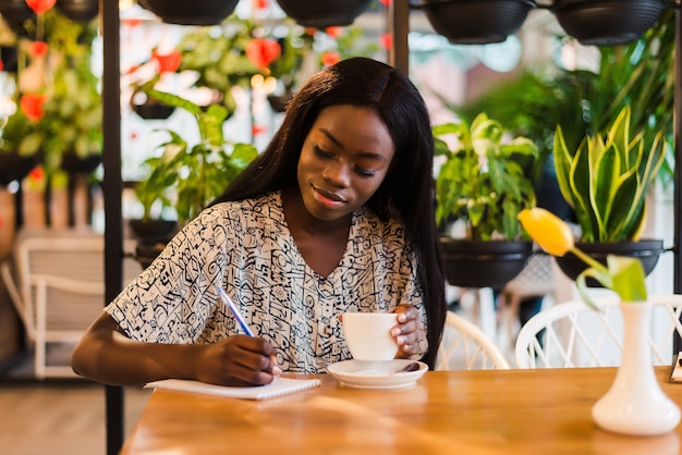 Retrato de joven y bella mujer africana sentada en el café y escribir notas