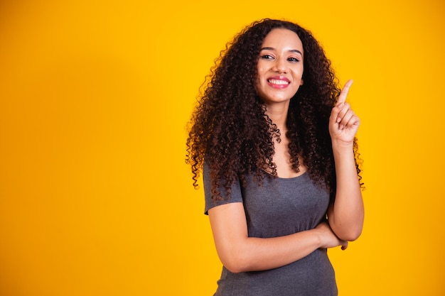 Retrato de joven y bella mujer afroamericana con cabello rizado pensando y teniendo una idea sobre fondo amarillo con espacio para texto. buena idea concepto de mujer