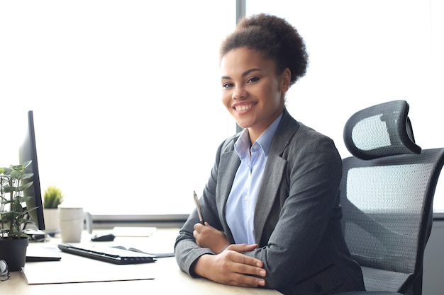 Retrato de joven y bella mujer afroamericana trabajando en equipo mientras está sentado en la mesa.