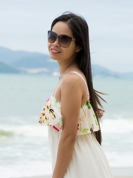 Retrato de joven bella mujer asiática con gafas de sol y de pie en la playa. Concepto de verano, relajación o vacaciones.